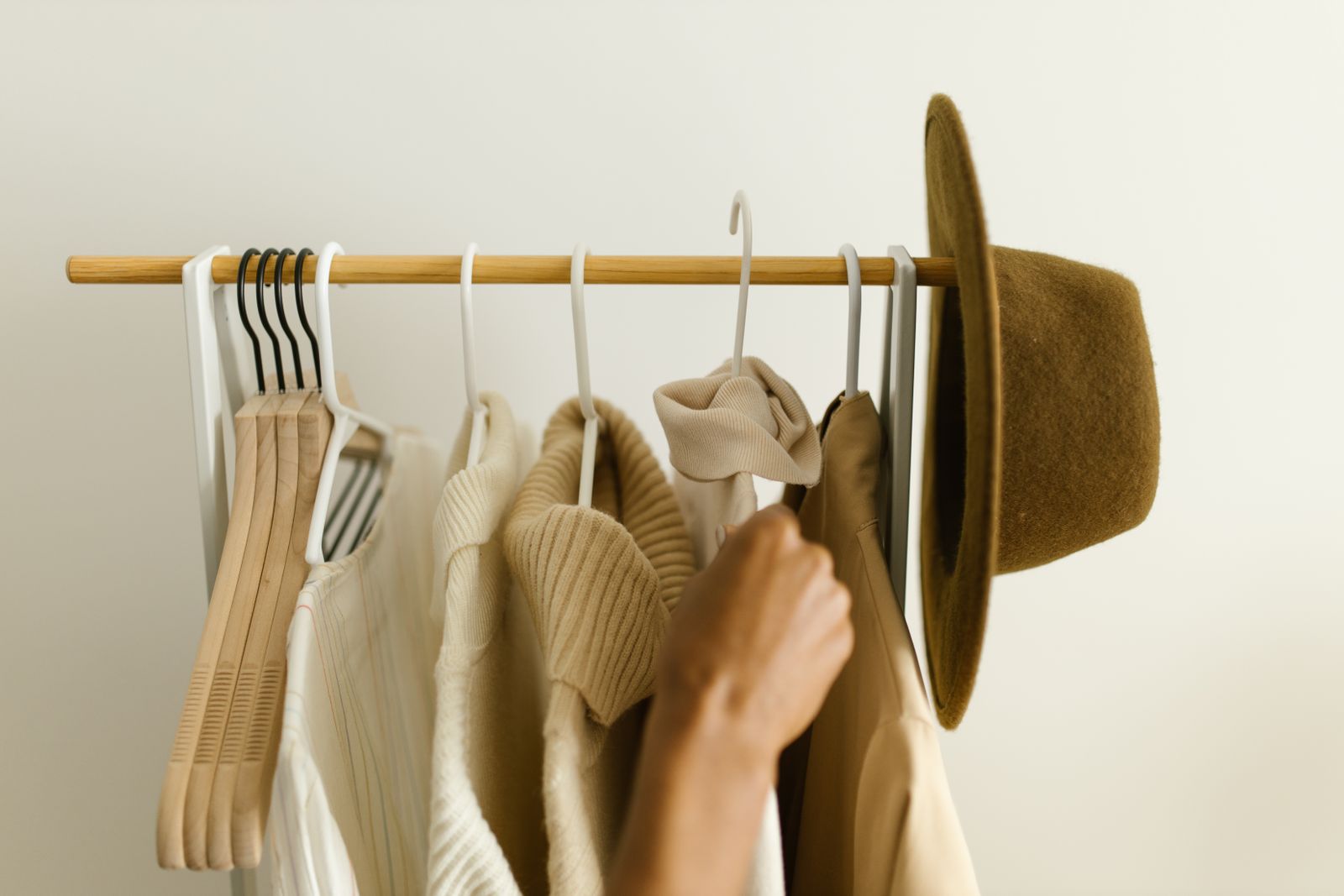 Mains qui choisissent un vêtement beige sur un portant, chapeau suspendu