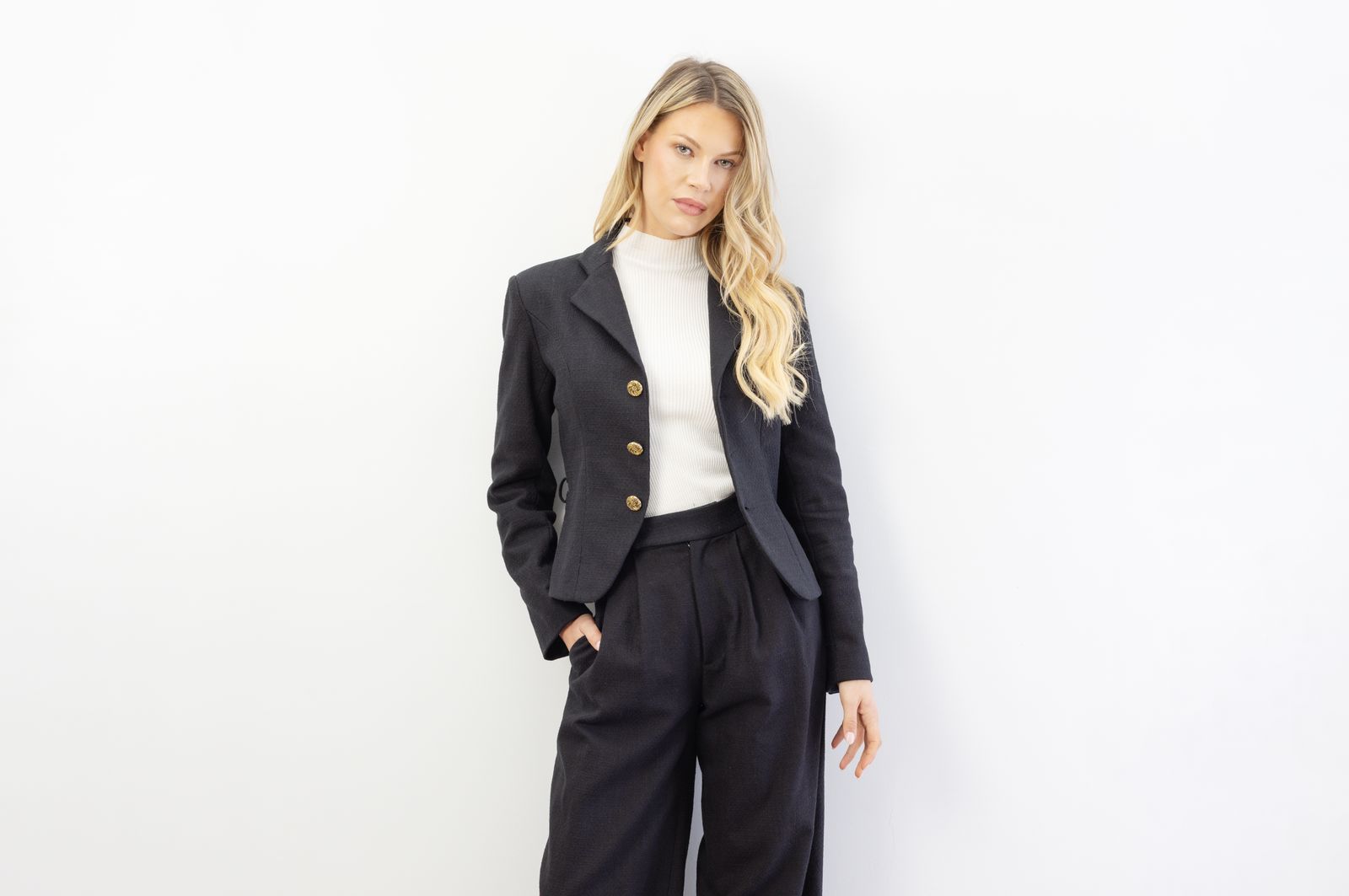 Femme en tailleur noir à boutons dorés, maille blanche et pantalon large à pinces